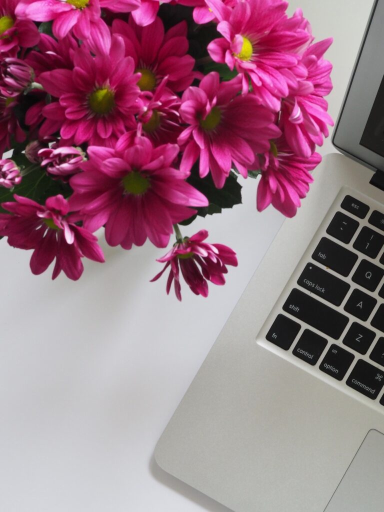 Laptop com ramo de flores cor de rosa ao lado.