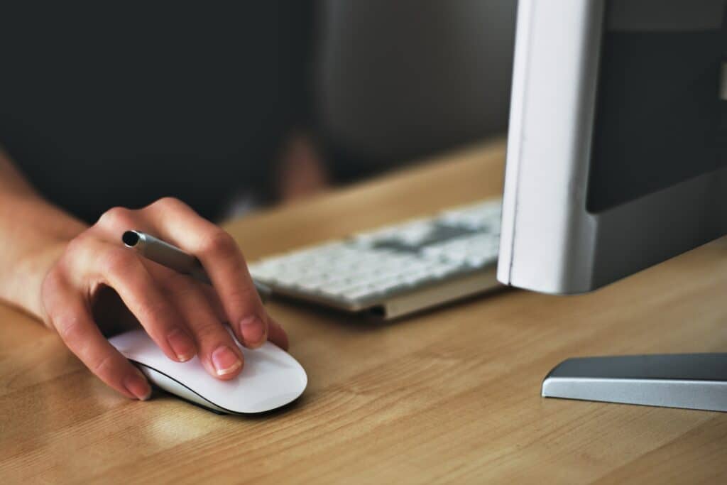 Mão com uma caneta e mouse operando um computador